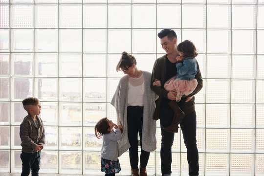 Family of five laughing together in front of window grid