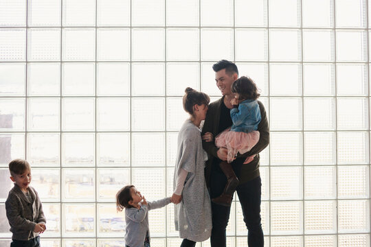 Family of five laughing together in front of window grid