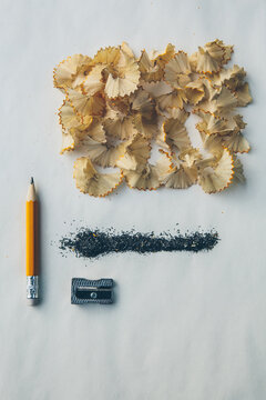 Deconstructed pencil with pencil shavings, graphite and pencil sharpener on top of paper