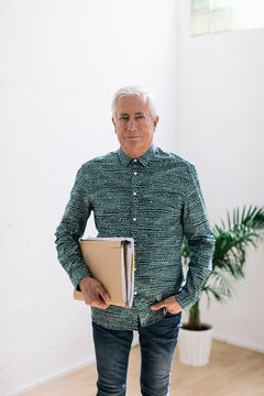 Portrait of an elderly businessman holding folders at office.