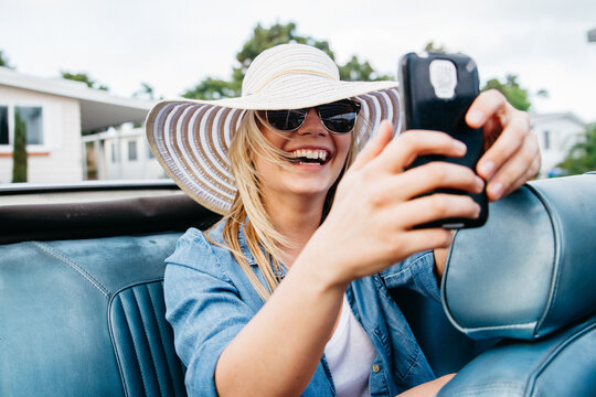 young teen female taking selfie in back of convertible car during summer