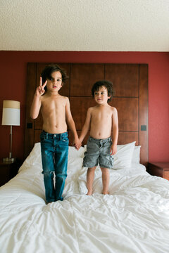 two little boys standing on a bed, flashing a peace sign