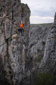 Man rock climbing a steep rock face on a cloudy day