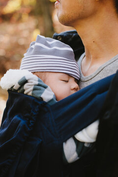 Little baby boy napping in a baby carrier worn by his dad