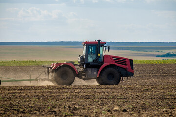 Fototapeta na wymiar A red farm tractor in a cloud of dust cultivates the soil in the field with a cultivator after harvest. Summer sunny day. Fertile land. Modern agricultural machinery. Copy space. High quality photo