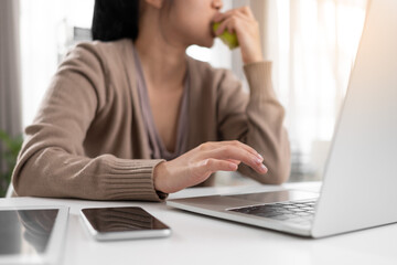 Young Asian woman using laptop for work with green apple