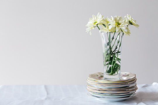 Vase filled with fresh daisies, sitting on a mismatched stack of china plates, with copyspace
