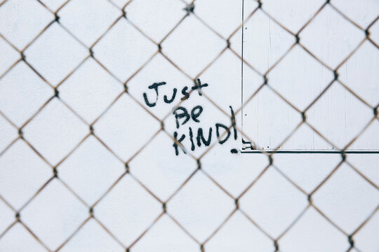 Graffiti written on white wall behind chain link fence