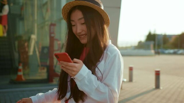 Good-looking cute chinese female tourist using cellphone navigating application exploring new city on summertime beautiful sunny day outdoors. Young woman. Travel concept.