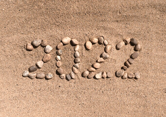 The numbers 2022 are written and lined with stones in the sand. Place for your text. Your text here.