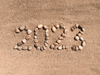 The numbers 2023 are written and lined with stones in the sand. Place for your text. Your text here.