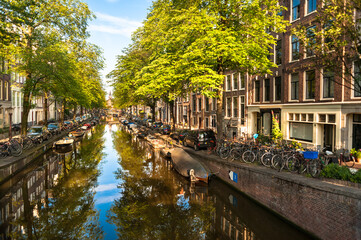 Sunny summer morning on Amsterdam Canal with boats and bicycles and houses