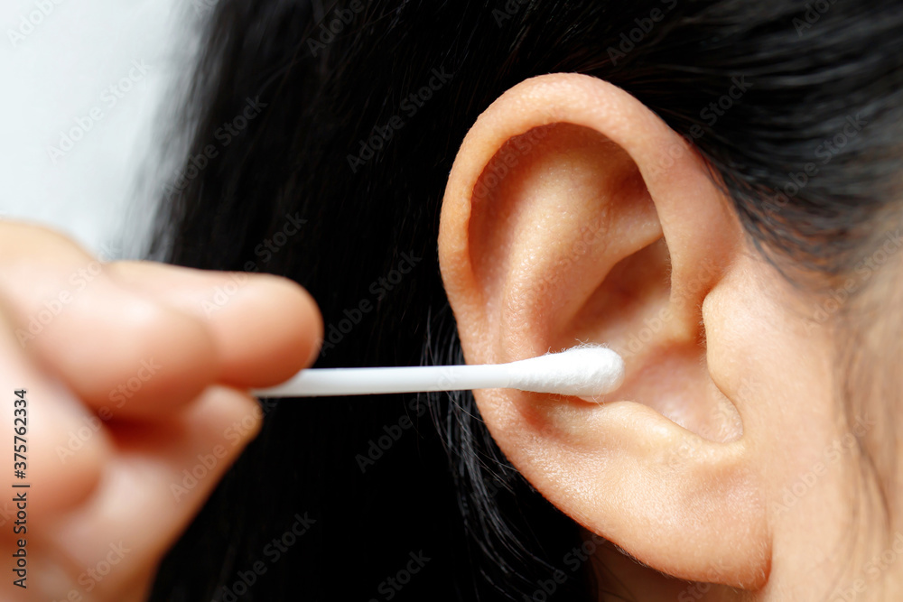 Wall mural close up female cleaning ear using cotton stick for Healthcare.