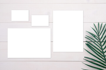 Blank paper sheet and name card mockup with copy space and leaf on wooden table, poster and invitation, postcard and business card decoration your design or branding, nobody, flat lay, top view.