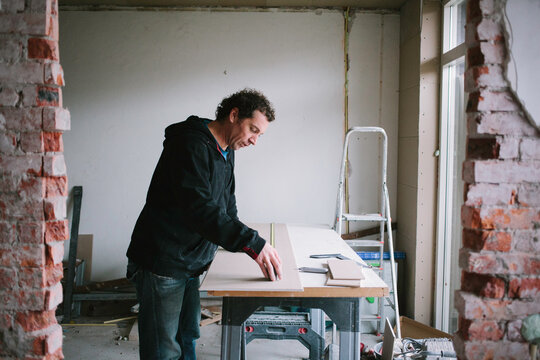 A man accurately measuring plasterboard while working on his workbench at home