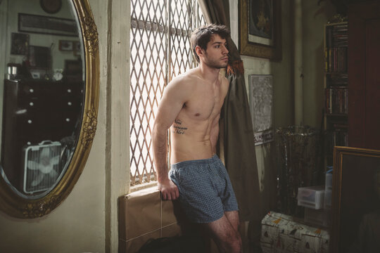 Man in Boxer Shorts Sitting by Window of Bedroom