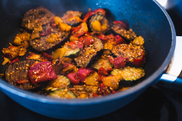 plant-based food, vegan eggplant zucchini and red pepper mix getting sauteed on a pan with mixed spices and fresh tomatoes