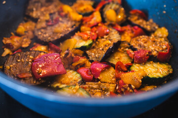 plant-based food, vegan eggplant zucchini and red pepper mix getting sauteed on a pan with mixed spices and fresh tomatoes