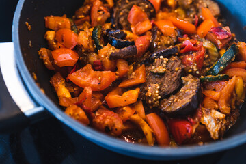 plant-based food, vegan eggplant zucchini and red pepper mix getting sauteed on a pan with mixed spices and fresh tomatoes