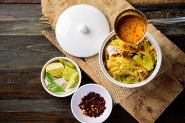 Northern Thai food (Khao Soi), Spicy curry noodles soup with chicken in a bowl eating with crispy deep-fried egg noodles, pickled mustard, shallots, lime and ground chillies fried in oil