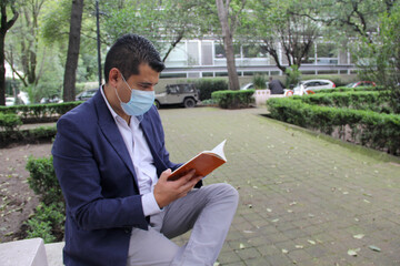 latin adult man with protection mask, reading book in park, new normal covid-19
