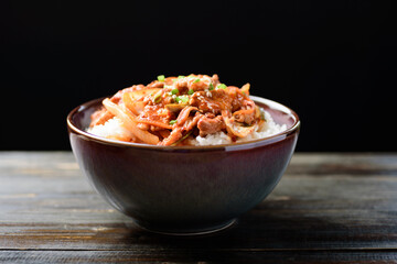 Stir fried kimchi with pork on cooked rice in a bowl on wooden background, Korean food