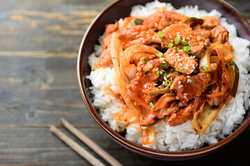 Stir fried kimchi with pork on cooked rice in a bowl on wooden background, Korean food