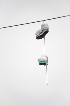 Shoes covered in snow hanging on electricity cable