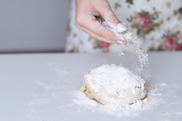 The hand of a young girl sprinkles flour on the cookie dough.