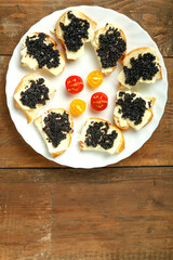 Sandwiches with black caviar on a white plate on a wooden table.