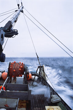A small boat under steam in open ocean with waves rolling over its deck