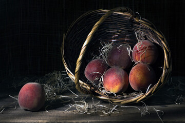 Still life with fresh peaches in a wicker basket on a wooden table.