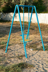 Blue baby swing on the beach with dried grass.