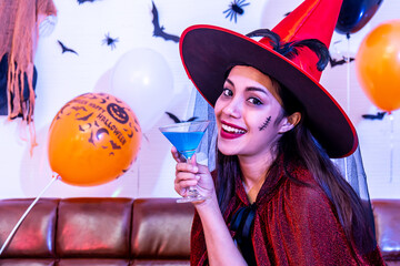 Beautiful asian young girl in witch costume having fun with cocktail drink alone at Halloween party by celebration, Pretty woman smiling and enjoying at home.