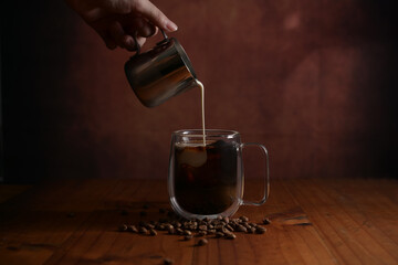 Close up view of barista pouring milk into a cup of coffee on wooden table
