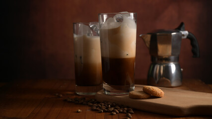 Two glasses of ice coffee with biscuit on wooden tray, coffee pot and coffee beans decorated on table