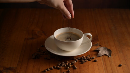 Close up view of barista hand adding coffee powder into cup on wooden table