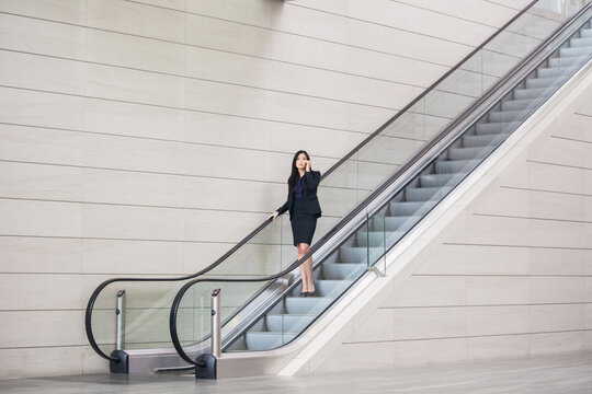 Asian businesswoman talking on her cell phone while going down on an escalator