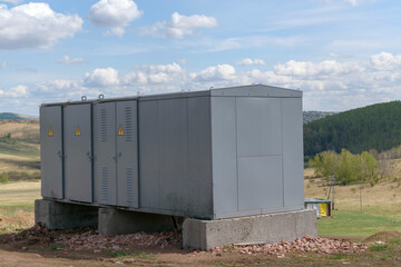 Mobile power distribution substation in Russia. A warning notice on the doors. Metal body. Green forest, clouds. The concept of power supply for remote industrial and residential.