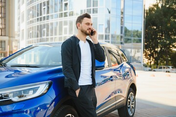 A handsome young businessman standing next to his car and talking on his phone