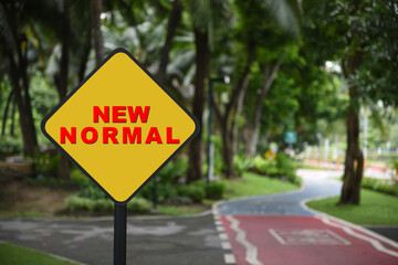 New normal word on yellow sign on bike lane background. Coronavirus disease 2019 or Covid-19 protect yourself concept and natural background idea