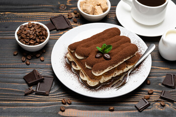 portion of Classic tiramisu dessert, cup of coffee and milk or cream on wooden background