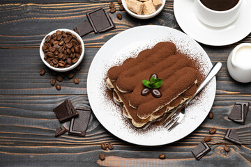 portion of Classic tiramisu dessert, cup of coffee and milk or cream on wooden background