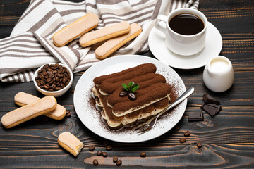 portion of Classic tiramisu dessert, cup of coffee and milk or cream on wooden background