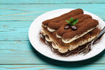 portion of Classic tiramisu dessert on ceramic plate on colorful blue wooden background