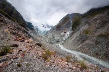Panoramic view from Robert's Point Track at Franz Josef Glacier melting into Waiho River and surrounded by mountain peaks covered in clouds in Westland Tai Poutini National Park in New Zealand.