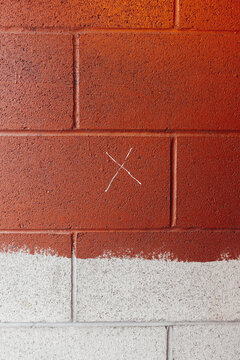 Brown paint covering graffiti markings on urban wall, small "X" in center