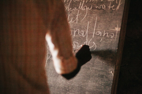 College-Aged Rwandan Boy Writes on a Blackboard