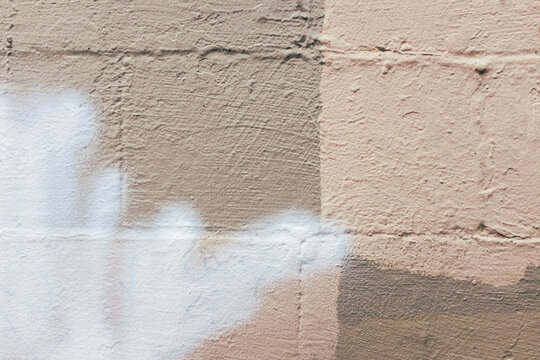 Brown and white paint covering graffiti tags on brick wall