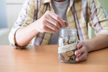 Selective focus at the glass jar. Men hand putting coin into glass jar full of coin saving for retirement pension fund.  Close up indoor shot with casual cloth. 
